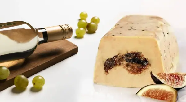 Bouteille de vin blanc à côté d'un bloc de foie gras aux figues, avec des raisins verts et des quartiers de figues. Un délice pour les amateurs d'alcool et de foie gras.