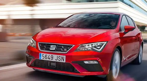 Czerwony Seat Leon 2025 pędzi po drodze, jego sportowy design przyciąga wzrok.