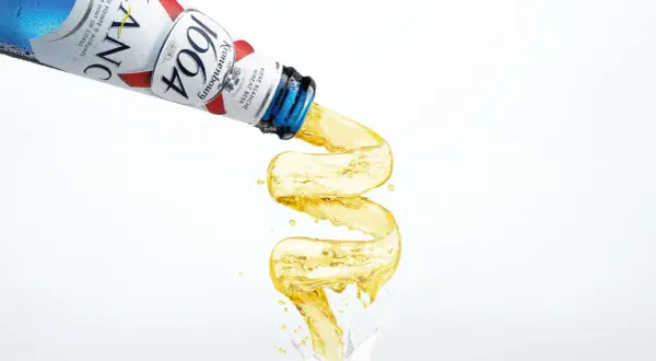Piwo w niebieskiej butelce Kronenbourg 1664 leje się w fantazyjny sposób, tworząc złoty strumień.