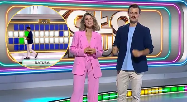 Prowadzący Koło Fortuny na tle planszy z literami i neonowych dekoracji.