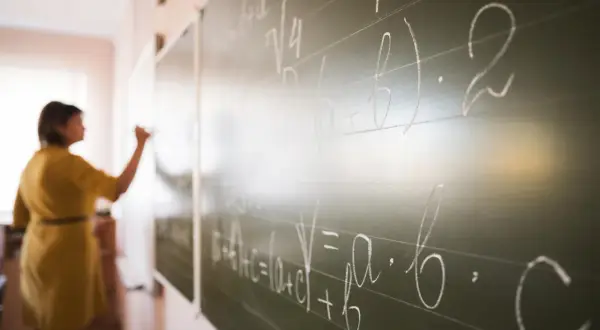 Nauczyciel dyplomowany pisze wzory matematyczne na tablicy.