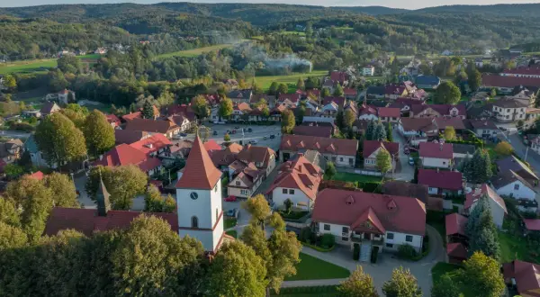 Widok z lotu ptaka na Lipnicę Murowaną. Widać kościół z wieżą, domy z czerwonymi dachami i otaczające lasy. To piękne miejsce oferuje wiele atrakcji.