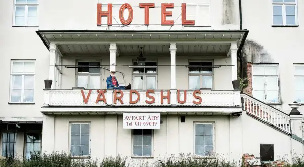 Man sitter på balkongen till ett gammalt värdshus med skylten "HOTEL VÄRDSHUS".