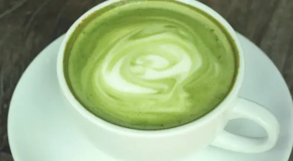 Zielony, spieniony napój w białej filiżance na spodku. To matcha latte, co to za napój?