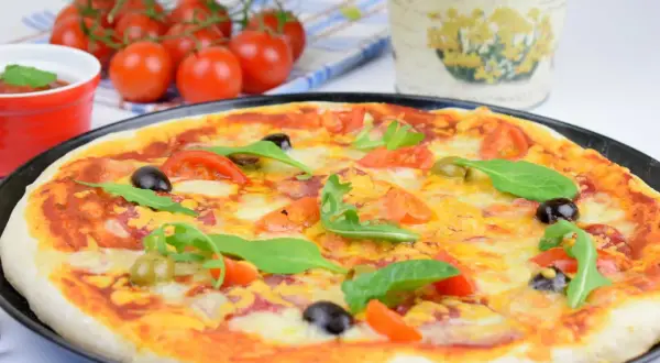 Domowa pizza z pomidorami, oliwkami i rukolą na czarnym talerzu.
