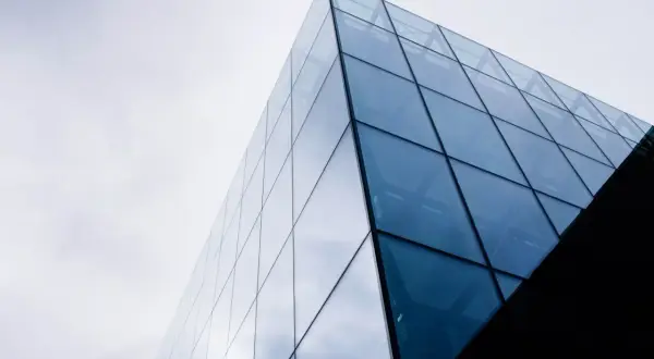 Nowoczesny budynek z geometrycznymi, błękitnymi szybami fotowoltaicznymi odbijającymi niebo.