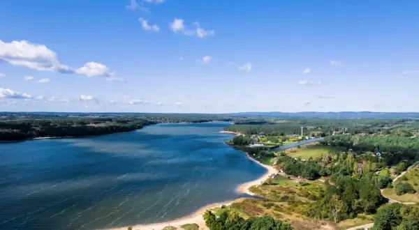 Malownicze jezioro Chańcza otoczone lasami, z piaszczystą plażą i zabudowaniami w tle.