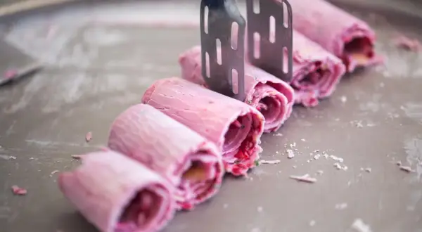 Eis selbst machen mit eismaschine: Rosa gerollte Eiscreme-Rollen werden mit zwei Spateln auf einer kalten Platte geformt.