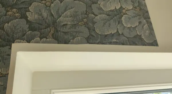 Detaljbild av en vägg med blått blommönster, visar hur tapetserar man runt ett fönster.