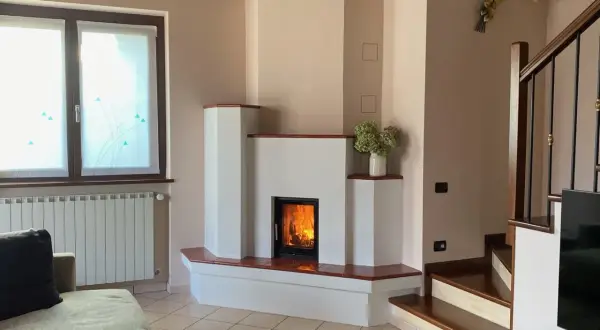 Camino moderno con fiamme vive. La struttura in **calce resiste alle alte temperature**, creando un angolo accogliente con scala e divano.