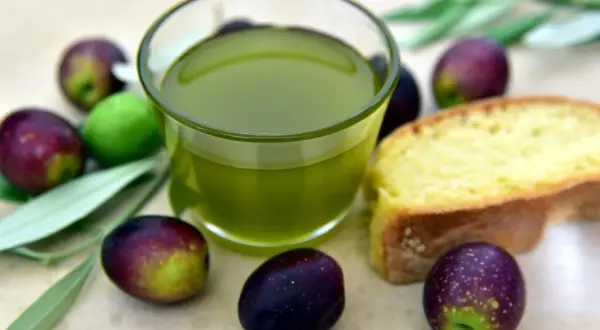 Olio extra vergine d'oliva e olive fresche, eccellenza dei prodotti DOP Puglia, accompagnati da una fetta di pane.
