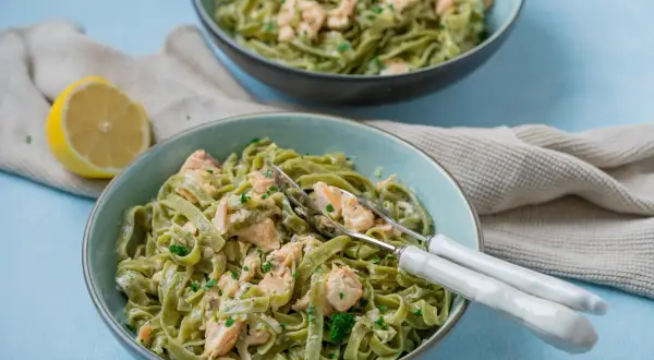 Zwei Schüsseln cremiger Tagliatelle al salmone, garniert mit Petersilie, daneben eine Zitronenhälfte und ein Küchentuch.