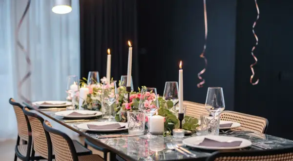 Tavola apparecchiata con candele, fiori rosa e bicchieri per un elegante servizio alla francese.