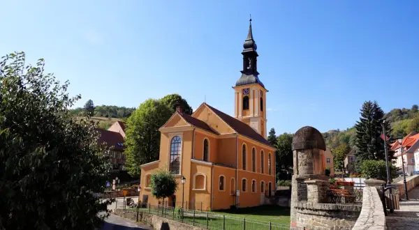 Pomarańczowy kościół z wieżą zegarową na rynku. W tle zielone wzgórza, przypominające srebrną górę.