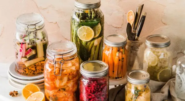 Eingemachtes Gemüse in Gläsern: Karotten, Gurken, Spargel, Kimchi und mehr. Was kann man nicht einkochen? Frische Kräuter und Zitronenscheiben geben Aroma.