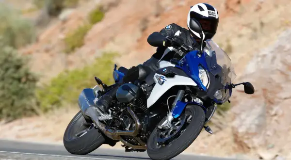 Motocyklista w kasku BMW śmiga na sportowym BMW RS 1200 po krętej drodze wśród pustynnych wzgórz.