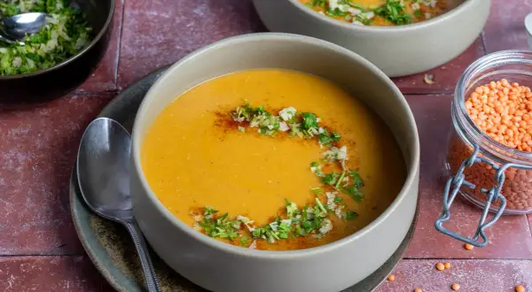 Herzhafte mercimek corbasi, eine cremige Linsensuppe, garniert mit frischen Kräutern und Gewürzen. Daneben eine Schale mit roten Linsen.