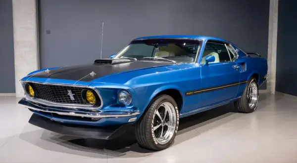 Błękitny Ford Mustang Mach 1 z 1969 roku, z czarną maską i żółtymi światłami, prezentuje się imponująco.