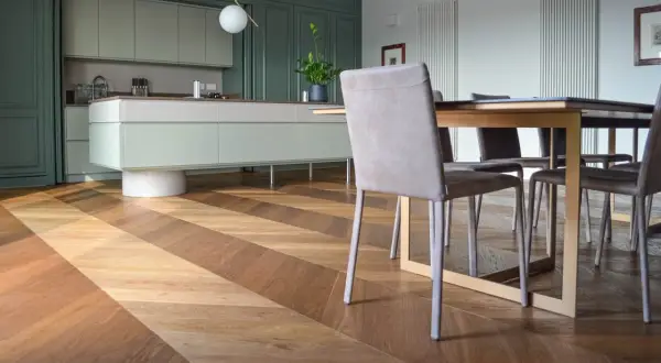 Un elegante parquet a spina di pesce in legno crea un motivo a zig-zag, che si estende dalla cucina moderna alla zona pranzo.