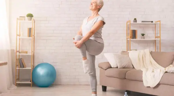Une femme âgée sourit en faisant un exercice d'équilibre, idéal pour une fiche technique gym douce pour personne âgée.