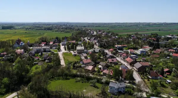 Widok z lotu ptaka na malowniczą wieś, która może pochwalić się mianem najmniejszego miasta w Polsce. Domy z czerwonymi dachami, kościół i zieleń pól tworzą sielski krajobraz.