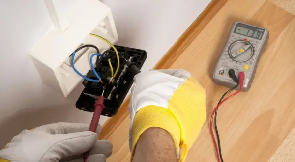 Elektryk sprawdza napięcie w gniazdku. Woltomierz służy do pomiaru napięcia elektrycznego, co jest kluczowe przy pracach instalacyjnych.