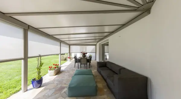 Telo per pergolato fissato con sistema a scomparsa, creando un'area relax con divano e tavolo da pranzo.