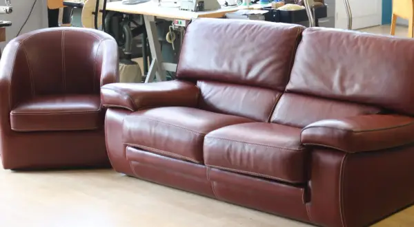 Un fauteuil et un canapé en cuir marron, avec des coutures blanches contrastantes, sont présentés dans un atelier.