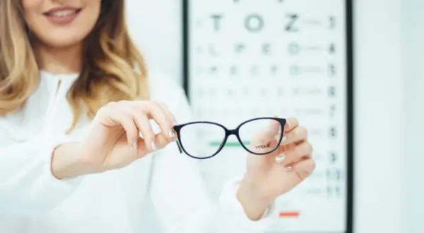 Okulary progresywne dla osób z astygmatyzmem. Optometrystka prezentuje okulary na tle tablicy Snellena.