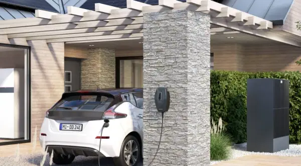 Ein weißes Elektroauto lädt an einer Ladesäule. Im Hintergrund ein modernes Haus mit Wärmepumpe und Solaranlage. Perfekt für die evu sperrzeit.