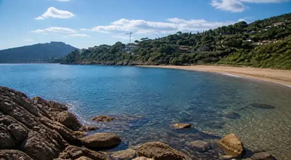 Baia tranquilla con acque cristalline e sabbia dorata, una delle splendide porto ercole spiagge, incorniciata da rocce e vegetazione lussureggiante.