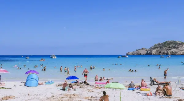 Słoneczna plaża na Majorce, pełna ludzi kąpiących się i opalających. Idealne miejsce na wakacje z dziećmi, oferujące mnóstwo atrakcji.