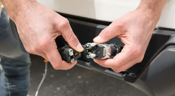 Mains de personne effectuant le branchement prise caravane. Connexion d'un connecteur électrique à une prise sur un véhicule.