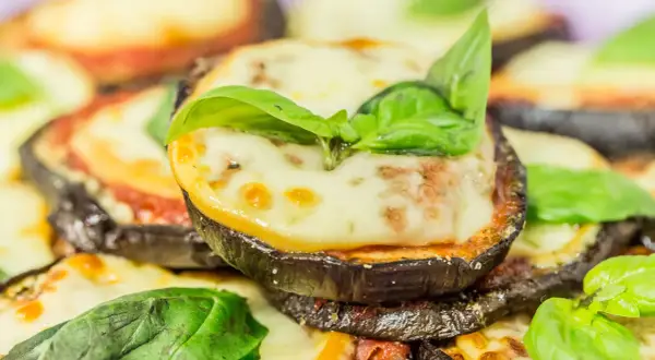 Fette di melanzane cotte al forno, ricoperte di sugo di pomodoro, mozzarella filante e basilico fresco. Un piatto invitante di melanzane alla pizzaiola.