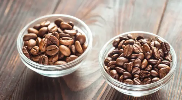 Due ciotole di vetro piene di chicchi di caffè tostati, una con chicchi più chiari, l'altra più scuri, per scegliere tra arabica o robusta.