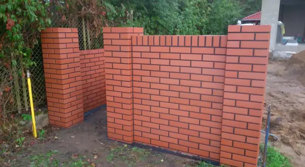 Nowy, solidny ogrodzenie z czerwonej cegły z czarnymi fugami, w trakcie budowy.