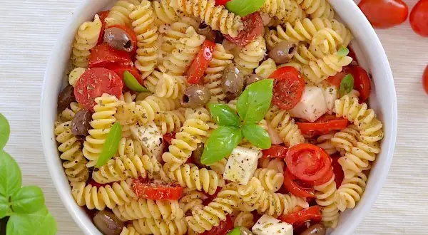 Un piatto invitante di pasta fredda con pomodorini, olive, cubetti di mozzarella e basilico fresco. Perfetta per un'estate gustosa.
