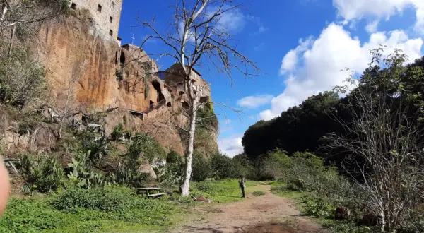 Sentiero verso Castel Sant'Elia, cosa vedere: roccia imponente, vegetazione rigogliosa e un cielo azzurro con nuvole bianche.