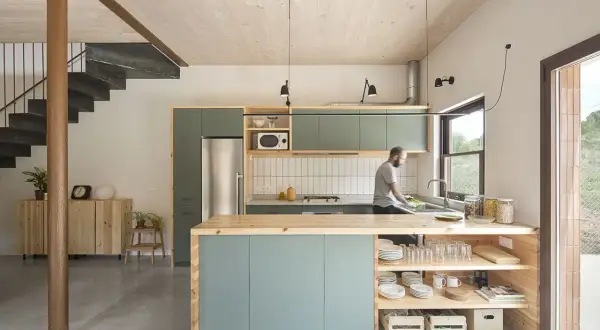 Hombre lavando platos en una cocina moderna y luminosa, ideal para renovar cocina con estilo minimalista y materiales naturales.