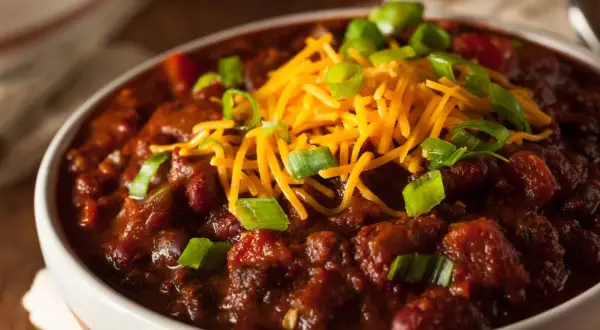 Gęste, aromatyczne chili con carne w białej misce, posypane startym serem i szczypiorkiem. Idealne na chłodne wieczory.
