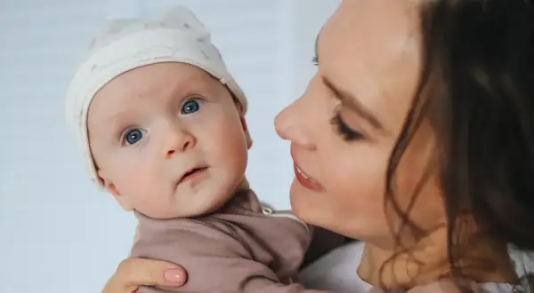 Mama z czułością tuli dziecko. Poradnik: jak nauczyć dziecko ssać pierś po butelce, by karmienie było łatwe i przyjemne.