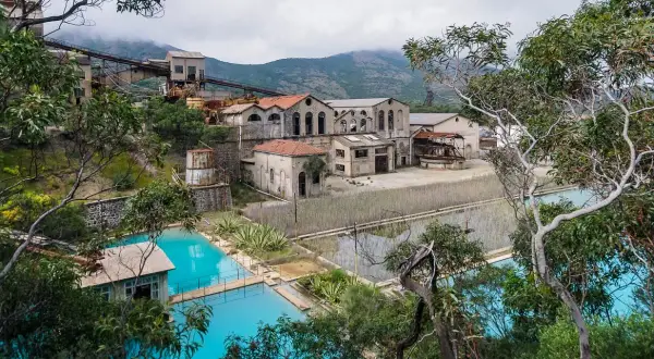 Antica zona mineraria sarda con edifici abbandonati e vasche d'acqua turchese.