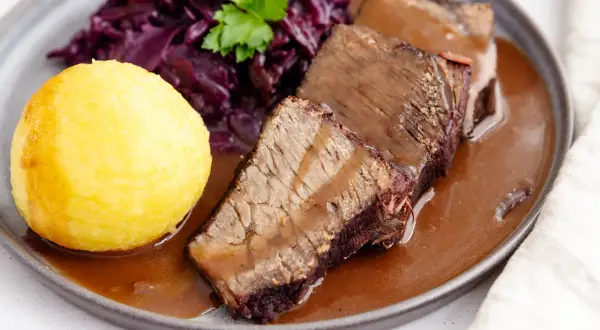 Original Sauerbraten: zartes Rindfleisch in dunkler Sauce, serviert mit Rotkohl und Klößen.