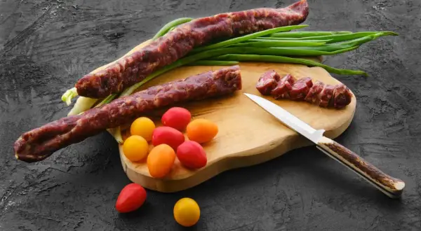 Dwa kabanosy, pomidorki i szczypiorek na desce. Czy koty mogą jeść kabanosy? Lepiej nie ryzykować.