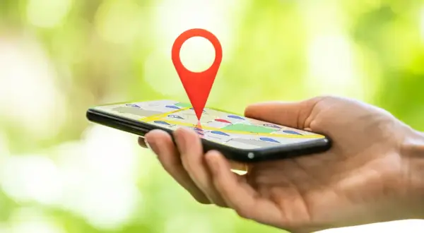 Dłoń trzyma smartfon z mapą i czerwoną pinezką. Dowiedz się, jak zlokalizować telefon przez Google.
