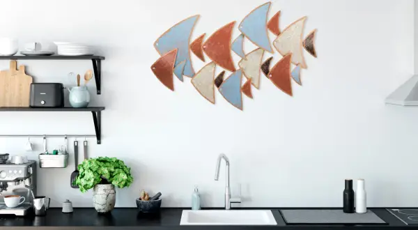 Décoration murale cuisine : un banc de poissons stylisés aux couleurs pastel et terreuses orne le mur blanc au-dessus d'un évier moderne.