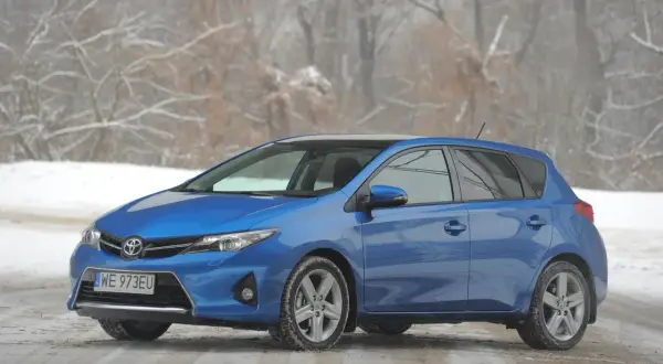 Niebieski Toyota Auris na śniegu, z widocznymi przednimi żarówkami.