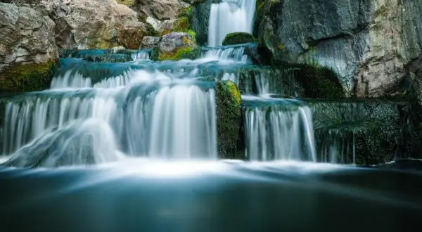 Serene waterfall photography captures cascading water flowing over moss-covered rocks, creating a tranquil, misty scene.