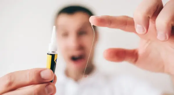 Zastanawiasz się, czym zmyć super glue z rąk? Oto mała nić, która przykleiła się do palca, obok tubki kleju.
