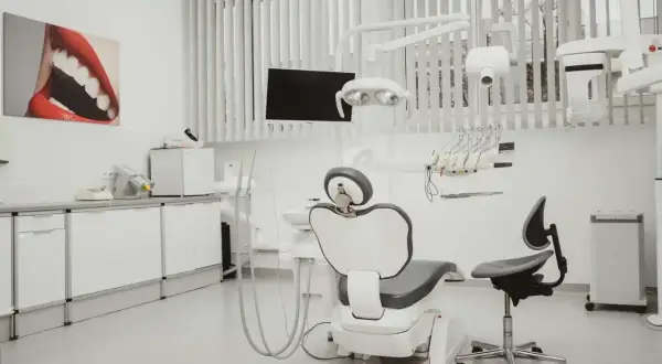 Nowoczesny gabinet stomatologiczny i ortodontyczny. Biały fotel dentystyczny, lampa, unit i szafki. Obraz z uśmiechem na ścianie.